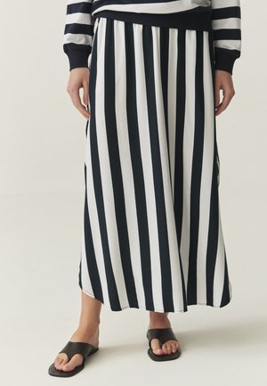 Falda maxi a rayas en blanco y negro con cinturilla elástica, combinada con sandalias negras planas. El tejido parece suave y fluido.