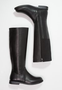 Botas de cuero negras hasta la rodilla con un acabado suave, que cuentan con una cremallera lateral y una suela de goma baja y plana. Incluyen un panel texturizado.