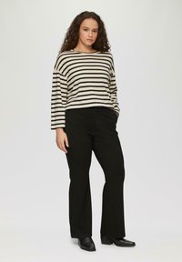 T-shirt à manches longues à rayures noires et blanches avec une coupe ample, associé à un pantalon noir évasé et des bottines noires. Design minimaliste.