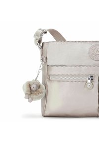 Metallisch hellbeige Tasche mit einer weichen Textur, ausgestattet mit einer Reißverschlusstasche und einem plüschigen Affenanhänger, der mit einer silbernen Kette befestigt ist.