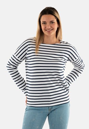 Maglietta a maniche lunghe con righe orizzontali blu navy e bianche, scollatura rotonda e vestibilità comoda. Abbinata a jeans azzurri.