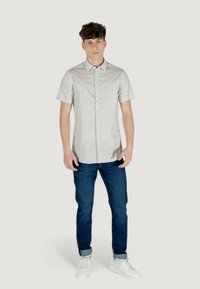 Camicia a maniche corte con bottoni di colore grigio chiaro con una texture a motivo sottile, abbinata a jeans blu scuro e sneakers bianche.