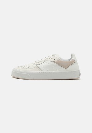 Niskie białe skórzane sneakersy z beżowym zamszowym detalem, wiązane z przodu, z perforowanym noskiem i grubą gumową podeszwą.