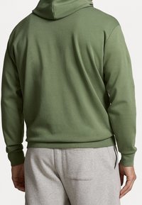 Zelená mikina s kapucí vyrobená z měkkého materiálu, s klokánkovou kapsou, žebrovanými manžetami a volným střihem, spárovaná se šedými tepláky.