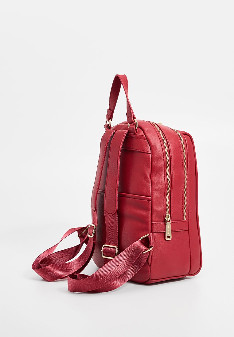 Bolso de cuero rojo con forma rectangular, dos cremalleras y correas ajustables. Presenta un acabado texturizado y acentos de hardware en tono dorado.