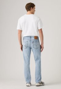 Hele sinised teksad kitsenevate sääreosade, keskmise kõrgusega vöökohaga ja pruuni nahast plaastriga tagumisel vööl. Valge T-särk ja hallid tossud.