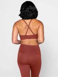 Brun sport-bh med korsade band, i kombination med högmidjade bruna leggings. Slät textur, minimalistisk design och inga synliga mönster eller varumärken.