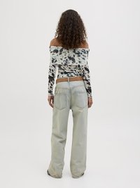 Top a spalla scoperta con maniche lunghe in un motivo tie-dye bianco e nero, abbinato a jeans a gamba larga blu chiaro con tasche posteriori e una cintura texturizzata.