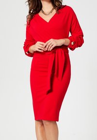Rotes Wickelkleid aus dehnbarem Stoff, mit langen Ärmeln und Cuff-Details, einem Bindegürtel in der Taille und einer taillierten Silhouette, die bis zum Knie reicht.