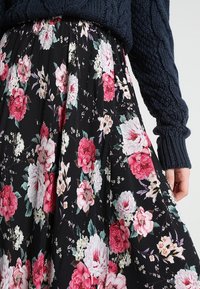 Mustat hameet, joissa on vaaleanpunaisia ja valkoisia kukkakuoseja, yhdistetty tummansiniseen neulepuseroon, jonka hihan päällä lepää käsi.