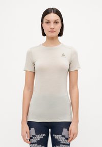 Īsām piedurknēm gaismas bežs sporta krekls, izgatavots no gludas auduma. Iezīmēts ar mazu logotipu uz krūšu un pieguļošu dizainu.