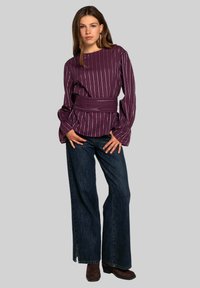 Blusa de manga larga a rayas moradas con cintura ajustada, combinada con vaqueros de pierna ancha oscuros y botines marrones. Textura suave y corte relajado.