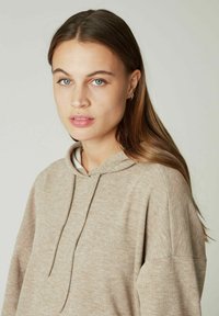 Felpa leggera beige con una texture morbida, cordino e maniche lunghe. Il design presenta una vestibilità rilassata e una leggera variazione di colore.