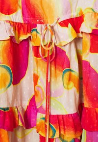Robe multicolore avec des motifs abstraits orange, rose et jaune. Fabriquée en tissu léger avec des volants et un détail à cordon.