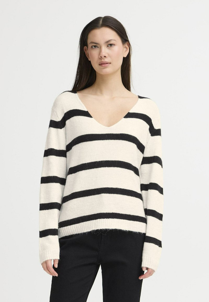 Striped knit sweater with a V-neck, featuring black and cream horizontal stripes, long sleeves, and a relaxed fit. Soft texture and ribbed cuffs.