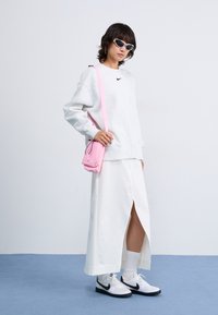 Grå fleece sweatshirt med sort logo, hvid maxiskørt med split, lyserød crossbody taske, hvide sneakers med sorte detaljer og solbriller.
