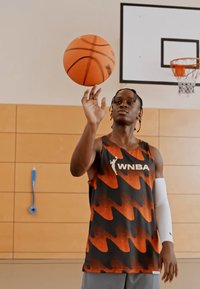 Sort og orange ærmeløs basketballtrøje med zigzag-mønster, logo på brystet og en hvid ærmemanchet. Spilleren drejer en basketball.