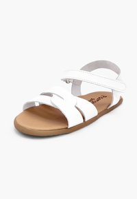 Sandale blanche avec deux brides à l'avant, une bride à la cheville avec fermeture à scratch, et une semelle plate couleur camel, vue en angle sur fond blanc.