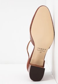 Chaussure à talon haut en cuir marron avec texture en relief crocodile, dos ouvert et talon effilé. Caractérisée par une semelle en caoutchouc plate et un marquage de la marque.