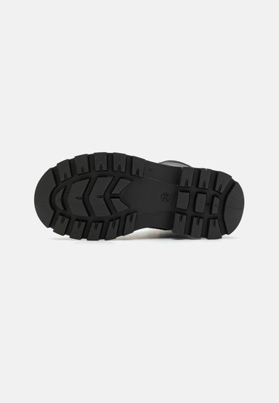 Semelle en caoutchouc noir avec un motif de semelle robuste, présentant des crampons profonds pour une meilleure traction. Surface lisse et design global solide.