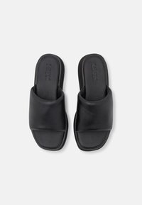 Black slide sandals with a wide crossover strap. Made of smooth leather with a flat sole, featuring minimal branding embossed on the insole.