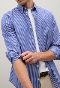 Chemise à boutons rayée bleue et blanche, manches longues retroussées jusqu'au milieu de l'avant-bras, tissu léger, poche poitrine simple, design de col classique.
