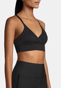 Bralette negro con escote en V, banda inferior ancha y tirantes delgados ajustables. Hecho de una tela suave y elástica con un diseño sin costuras.