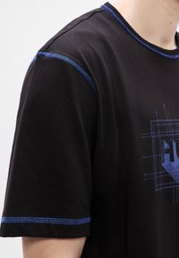 T-shirt preta com costura azul ao longo da gola e das mangas, com um desenho gráfico azul na frente e uma textura macia de algodão.