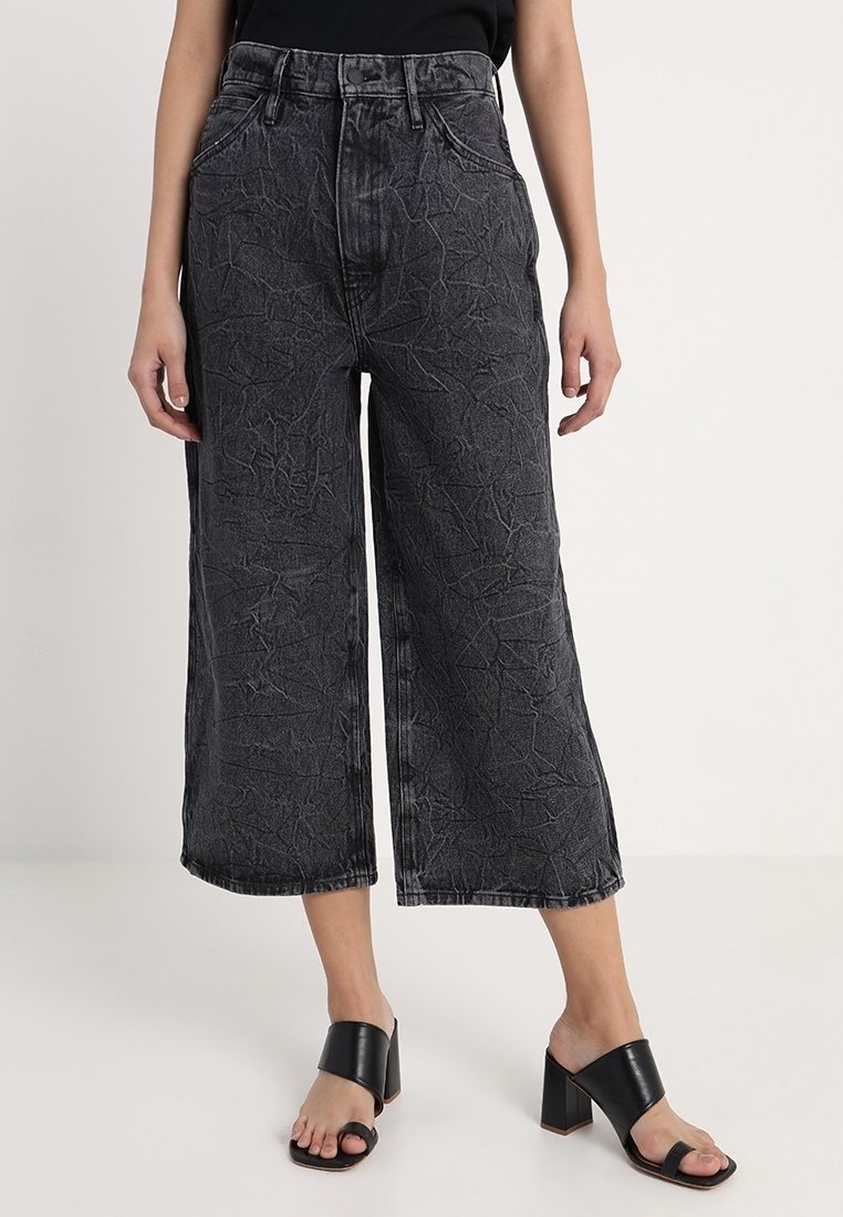 Sorte cropped denimbukser med struktureret overflade, højtaljede og med vidt ben. Kombineret med sorte sandaler med blokhæl.