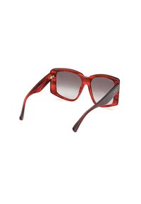 Punaiset muoviset aurinkolasit, joissa on neliömäinen kehys, liukuväriset linssit ja tyylikkäät sarvet. Huomionarvoisia modernista muotoilustaan ja kiiltävästä pinnastaan.