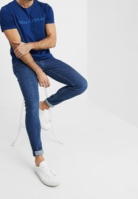 Námořnická modrá tričko s světle modrým logem, slim-fit džíny a bílé tenisky. Otočené manžety a minimalistické designové prvky.