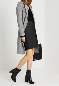 Grå rutig kappa, svart blus med volanger, figurnära svart kjol och svarta klackade ankelstövlar med nitar. Svart handväska ingår.