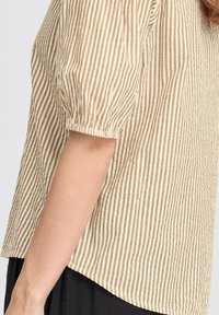 Beige og brun stribet bluse med puffede korte ærmer, lavet af letvægtsstof med struktureret overflade og buet kant.