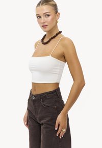Top tank blanc court avec fines bretelles, associé à un jean marron foncé taille haute. Accessoirisé avec un collier en perles marron et des bagues.