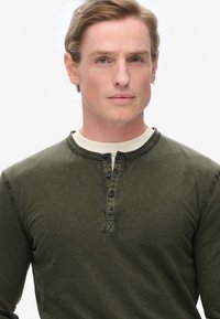 Langarmige groene katoenen henleyshirt met een ronde halslijn, een drieknoopsluiting en een subtiele textuur.