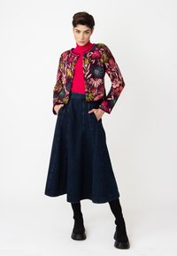 Kavaj med blommönster och en figursydd silhuett, kombinerad med en enfärgad rosa ribbstickad topp och en mörk denim A-linje kjol, avslutad med knähöga svarta stövlar.