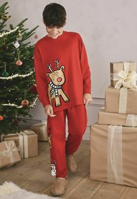 Rød bomulds pyjamas sæt med et rensdyr grafisk design på toppen og bunden. Blød tekstur, elastiske manchetter og matchende hjemmesko.