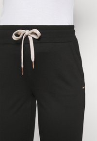 Zwarte sweatpants met een relaxte pasvorm, voorzien van een beige trekkoordsluiting met gouden uiteinden en een klein logo-accent op het been.
