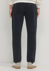 Pantaloni in velluto a coste blu navy con design a gamba dritta, caratterizzati da una texture liscia e un leggero luccichio. Indossati con sneakers bianche e dettagli beige.