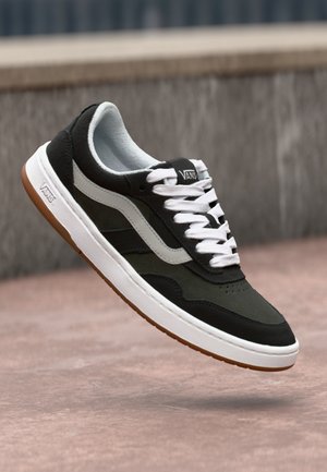 Baskets noires et vert foncé avec des lacets blancs, des accents gris et une surface texturée. Présente une semelle intermédiaire blanche et une semelle extérieure en caoutchouc naturel.