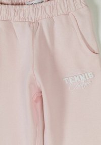Pantalon à taille élastique rose clair avec poches latérales et texte blanc "Tennis Centre" sur la cuisse supérieure.