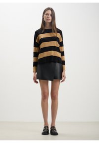 Maglione a righe nero e oro con una vestibilità rilassata, abbinato a una gonna avvolgente in pelle nera e mocassini in vernice nera con dettagli dorati.