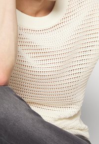 Top de punto en color blanco roto con un patrón texturizado de tejido abierto y cuello de canalé. Parte inferior con tejido gris.