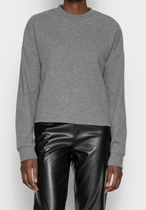 Person wearing a long-sleeve gray sweater and black leather pants, standing against a plain white background.