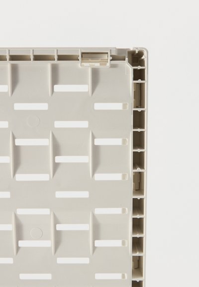 Panel de plástico gris claro con ranuras rectangulares y patrón de rejilla reforzado sobre un fondo blanco, mostrando un primer plano de los detalles estructurales.