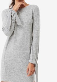 Vestido de punto gris con mangas largas, con lazos laterales en los puños. Ajuste regular con una textura suave para mayor comodidad.