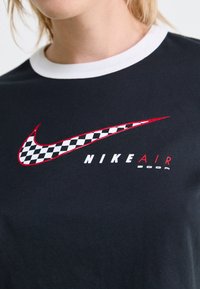 Musta puuvillapaita, jossa on valkoinen kaulus, punaisilla ruudullisella Nike-tuulettimella ja "NIKE AIR" -teksti valkoisena ja punaisena.