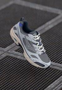 Gray and white athletic shoe with mesh material, a rounded toe, and blue accents. Features white laces and a textured, cushioned sole.