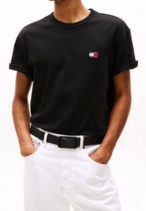 Czarny t-shirt z krótkim rękawem z podwiniętymi mankietami, z małym wielokolorowym logo "Tommy Jeans" na piersi, zestawiony z białymi spodniami i czarnym paskiem.