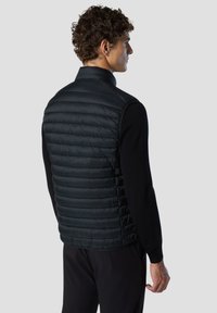 Chaleco acolchado negro con un collar estructurado, que presenta secciones acolchadas horizontales, tela lisa y una silueta ajustada.